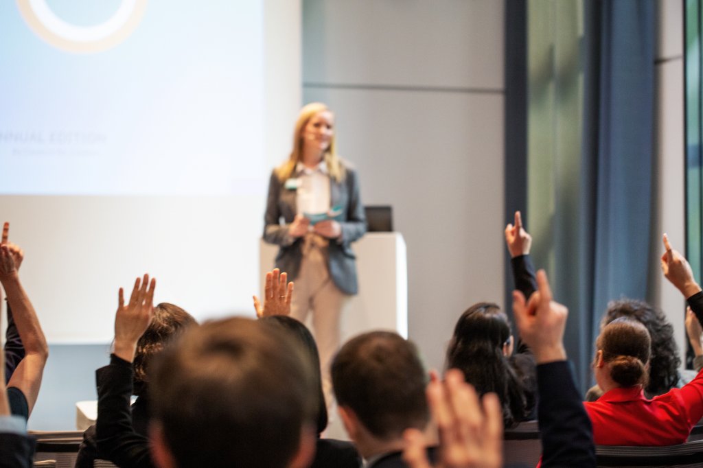 A woman giving a presentation to an audience all who have raised hands.