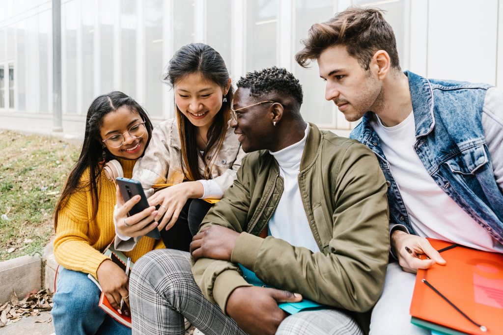 A group of four students looking at a mobile phone.